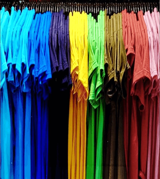 A vibrant display of folded t-shirts arranged in gradient colors, including blue, purple, yellow, green, brown, and pink